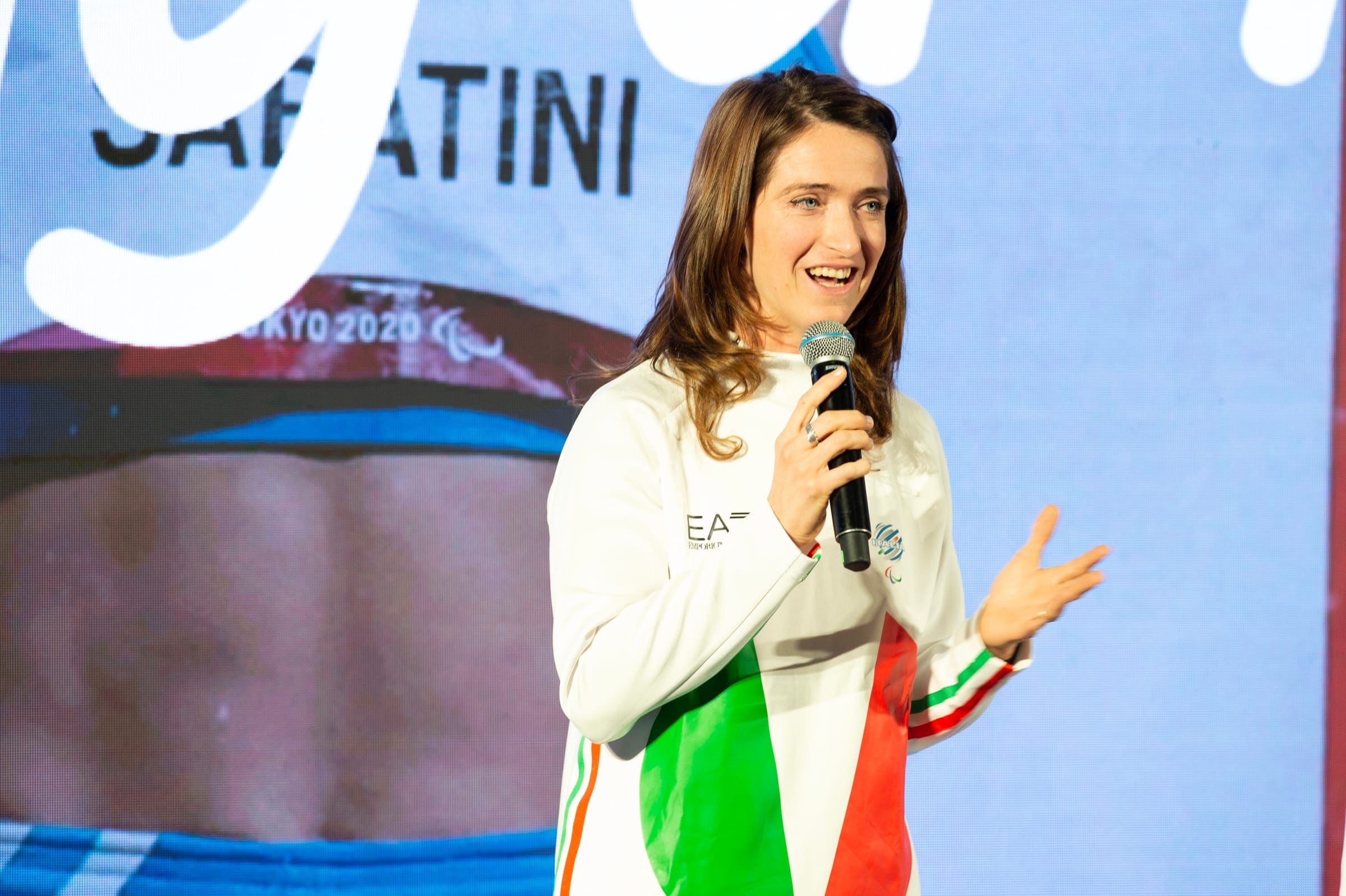 Martina Caironi speaks into a microphone in the Italian team's white tracksuit at Meet Milano Cortina 2026 in 2023
